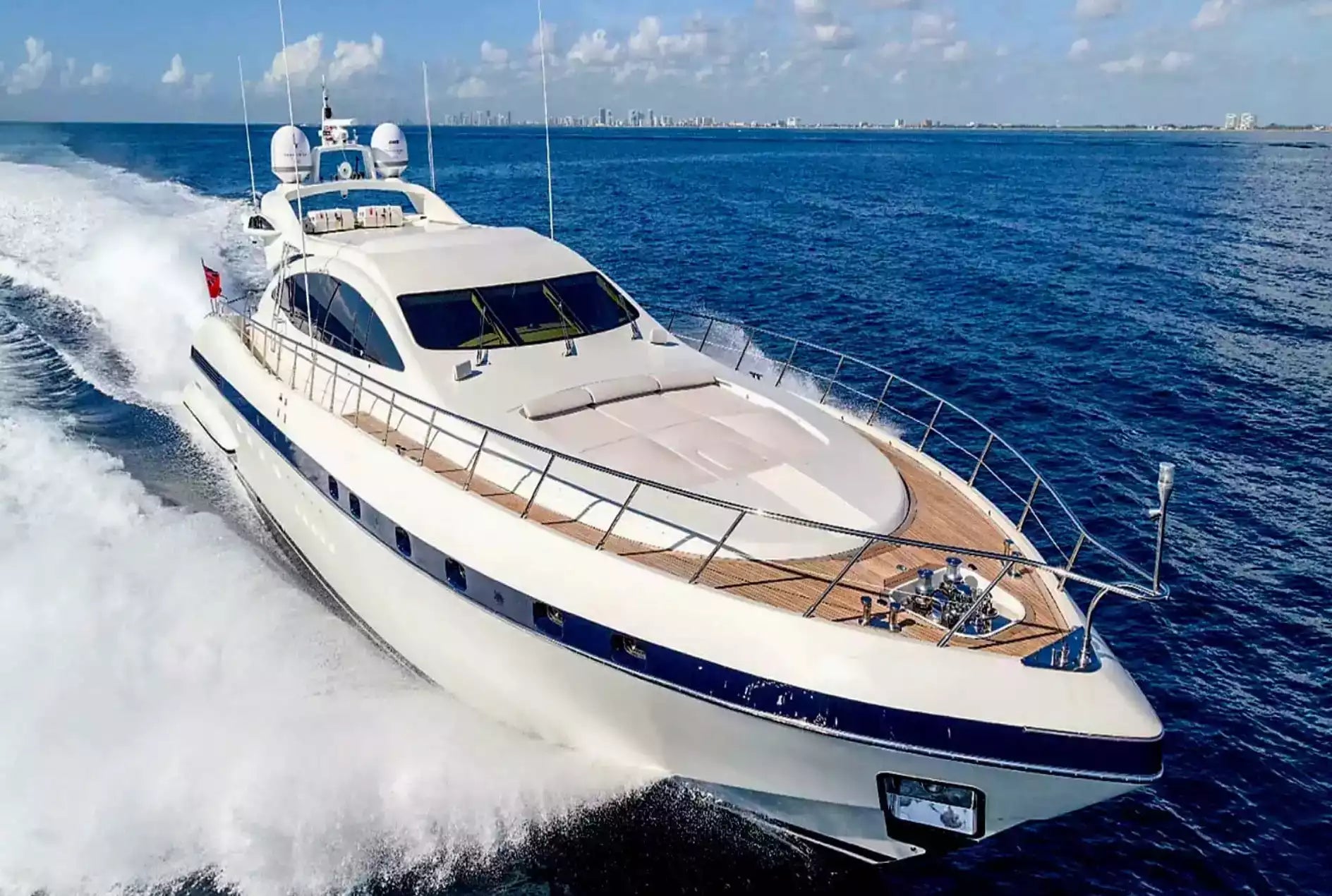 Luxury yacht speeding across the ocean with a city skyline in the distance.