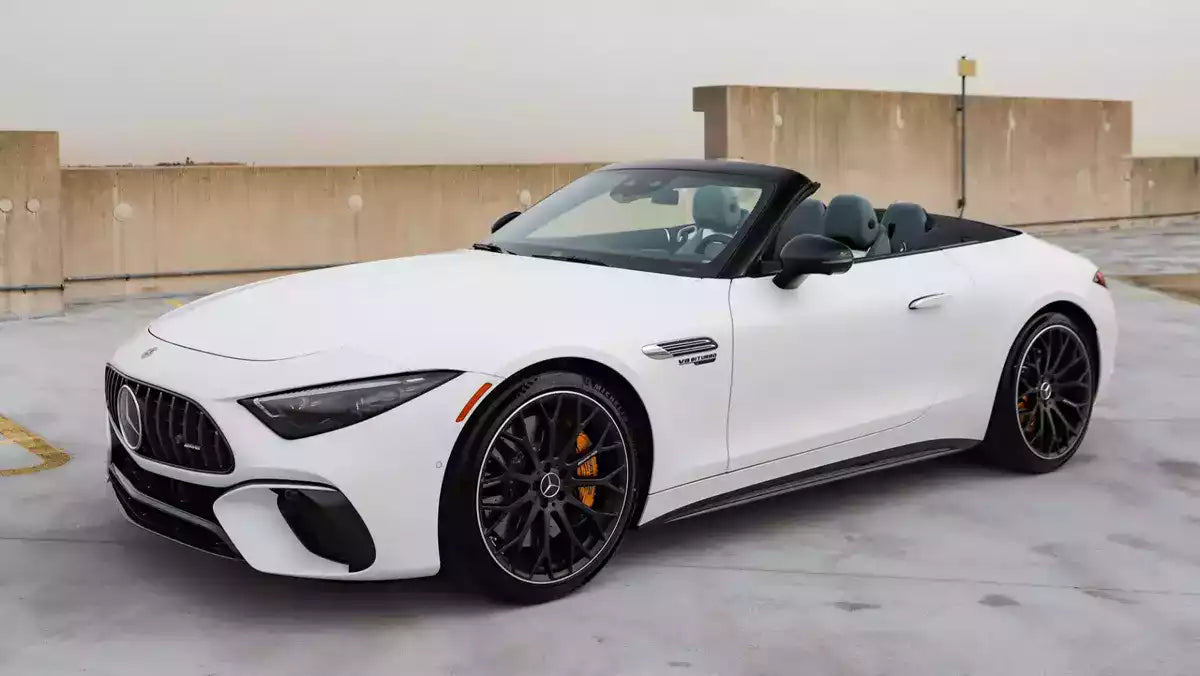 A white Mercedes-Benz Mercedes-AMG GT R convertible sports car parked on a concrete rooftop with a beige wall in the background.