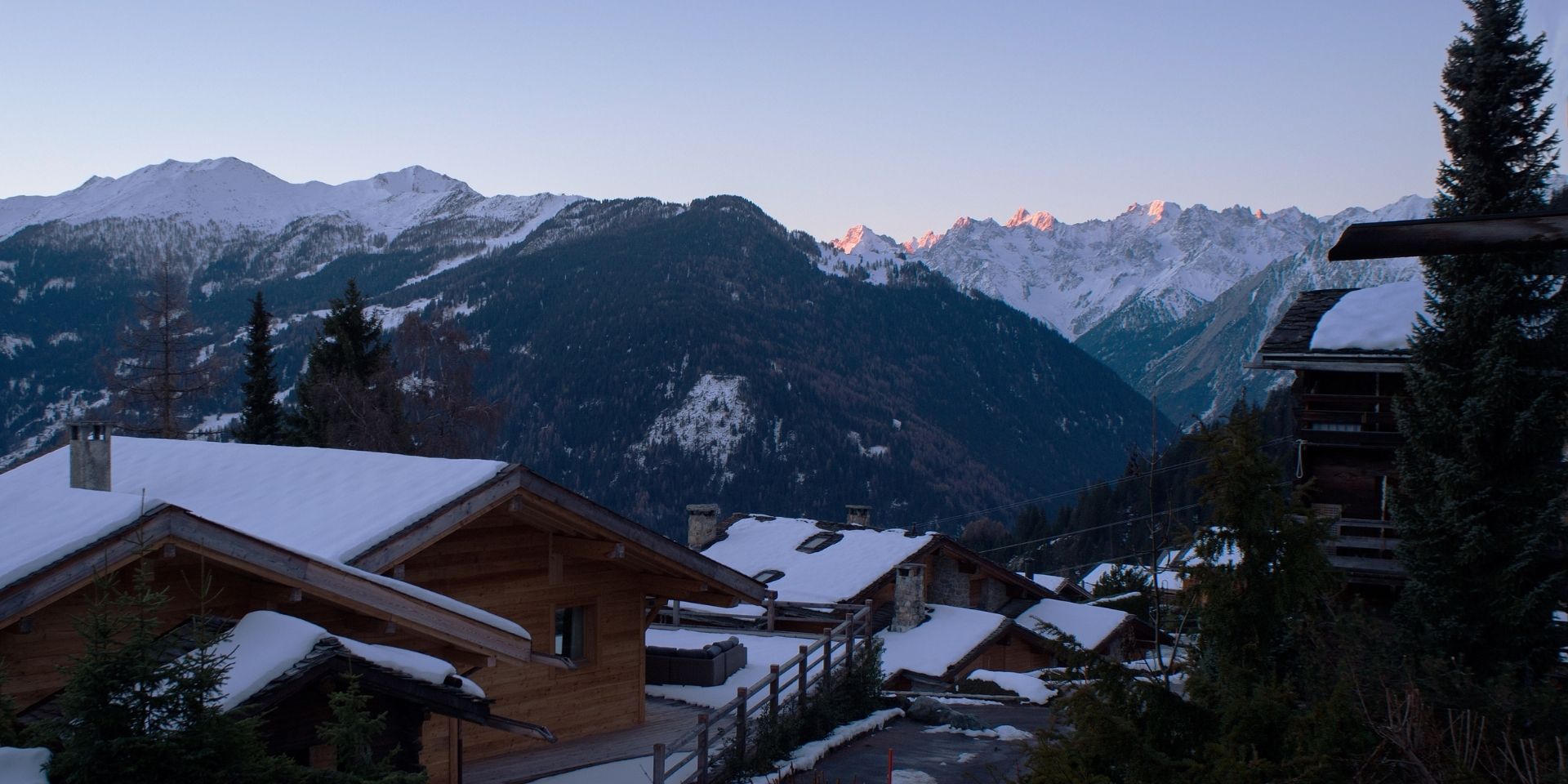 Snow-covered mountain village with wooden chalets at dusk.