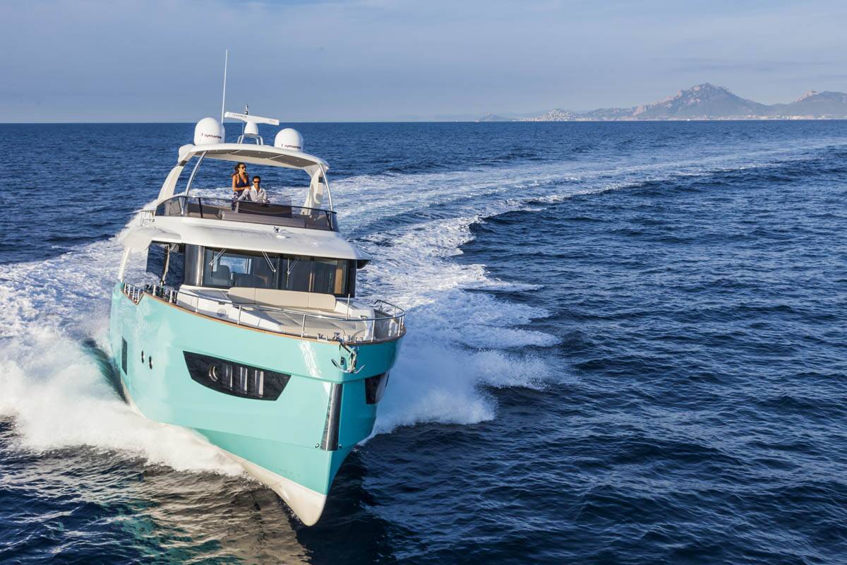 A luxury motor yacht in mint green and white speeds across deep blue ocean water, leaving a white wake behind it under a clear sky.