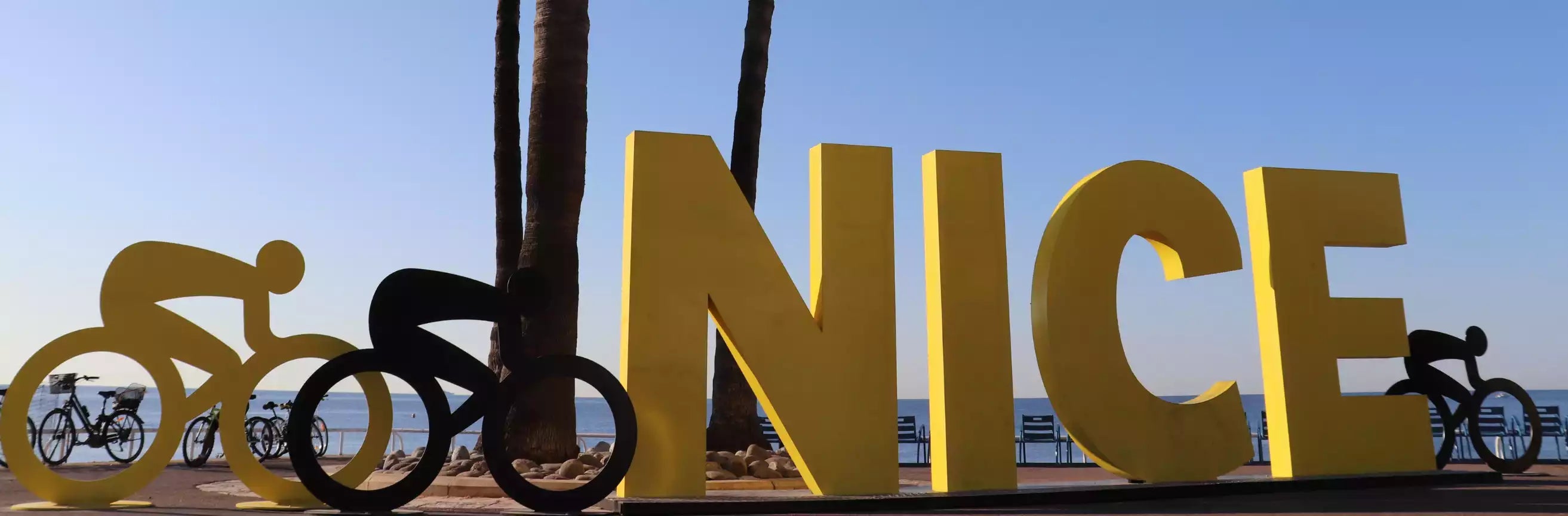 Large yellow letters spelling 'NICE' with bicycle sculptures in front of a palm tree and beach.
