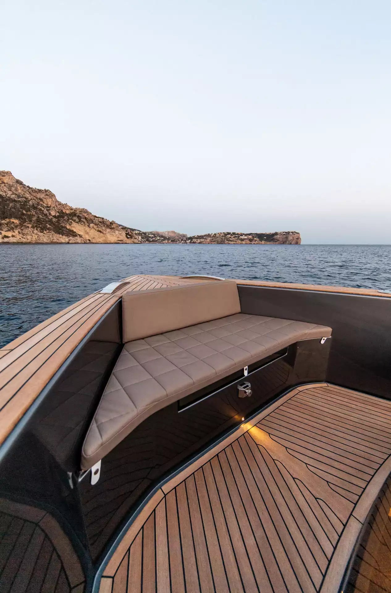 Boat interior with a cushioned bench seat on a body of water with mountains in the background