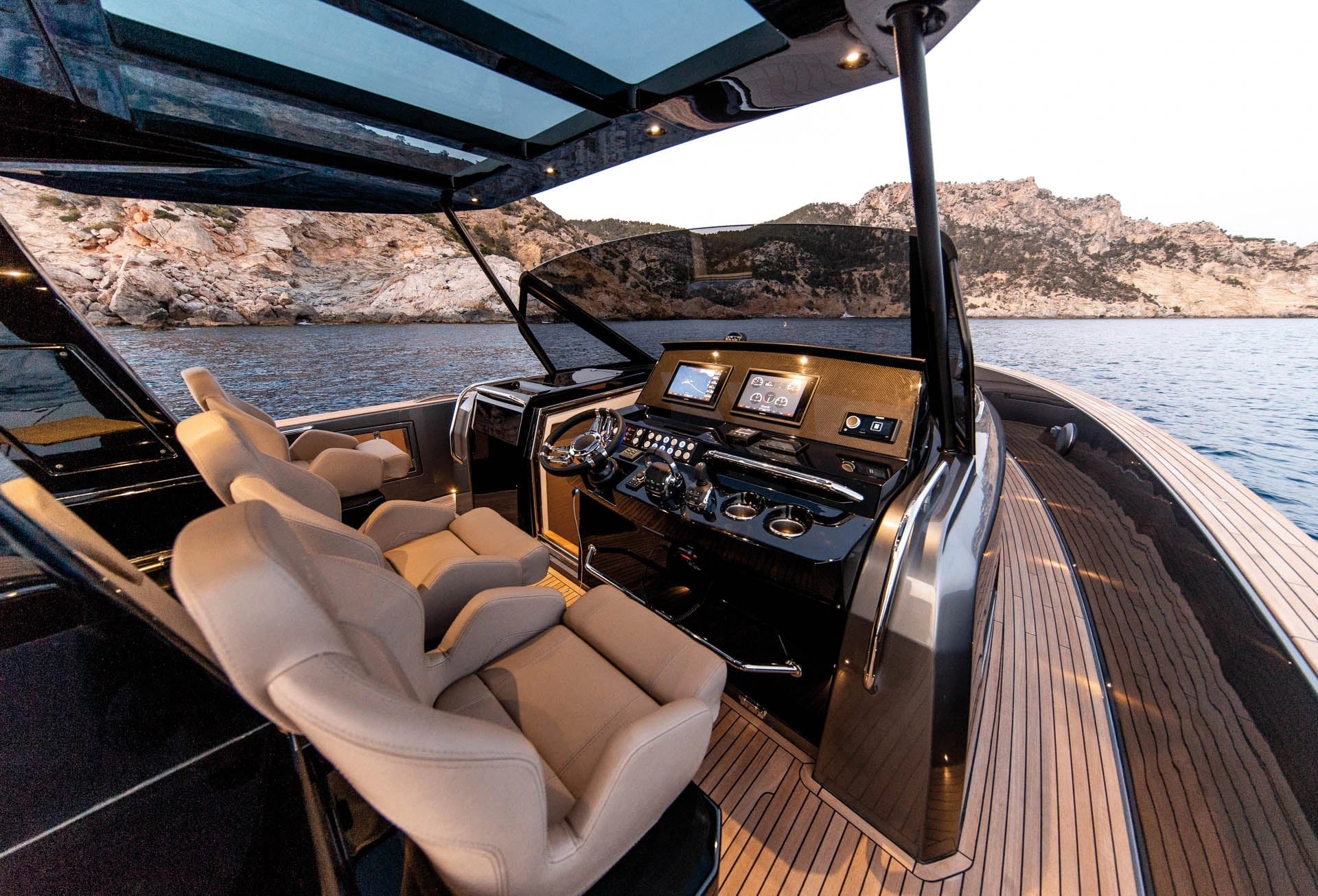 Luxury yacht interior with control panel and seating area, surrounded by water and mountains.