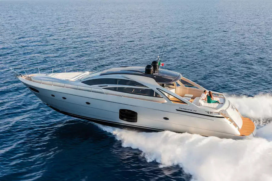 A luxury motor yacht with a white hull and tan deck accents, captured from an aerial perspective as it cuts through blue ocean water, leaving a white wake behind it.