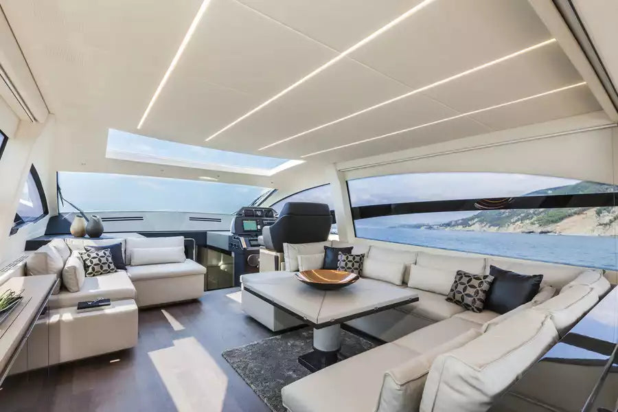 Luxury yacht interior with a modern U-shaped cream sofa, a matching coffee table, patterned accent pillows, and large windows overlooking the sea.