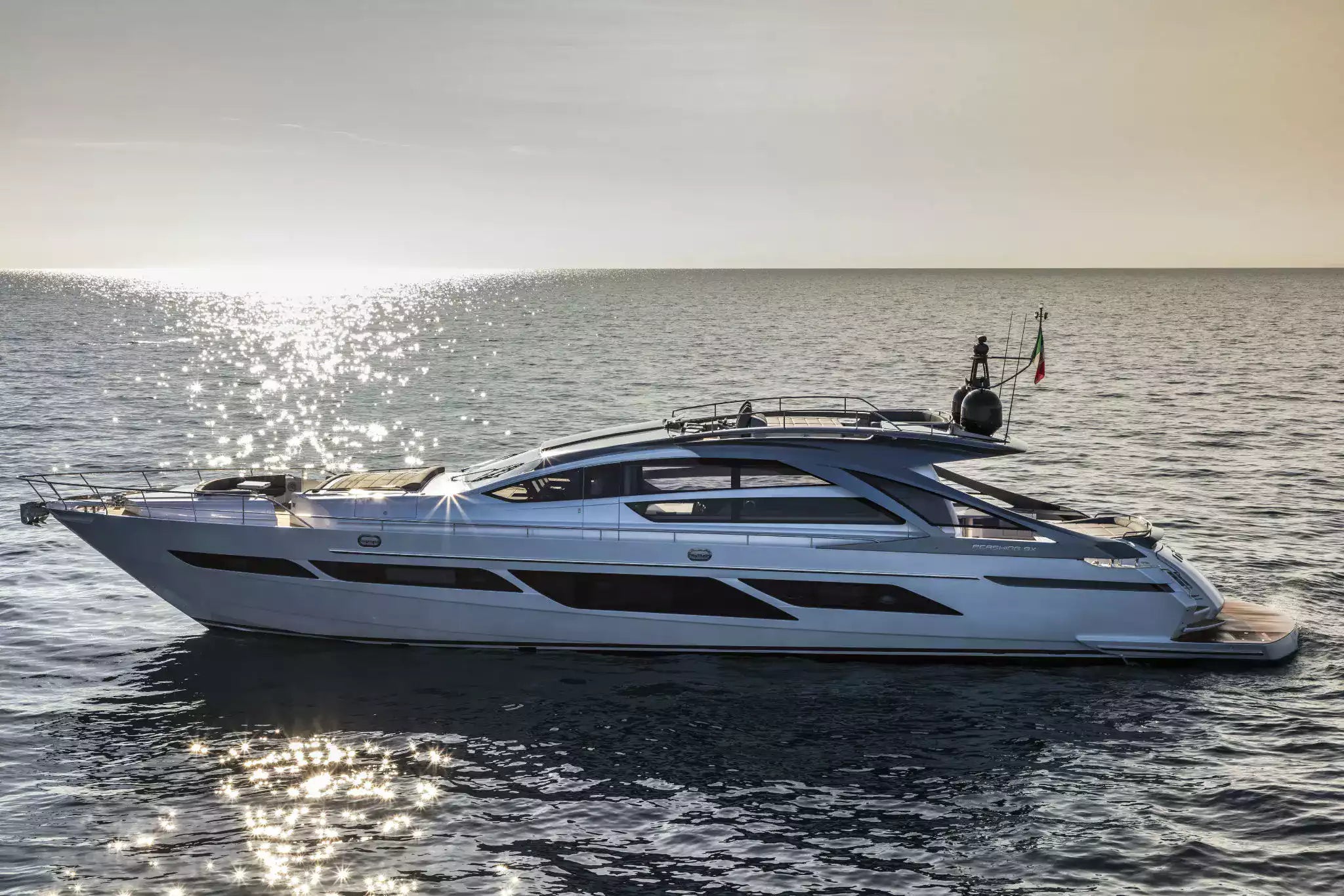 A luxury motor yacht with a white hull and dark gray superstructure floating on calm ocean water under a bright, sunlit sky.