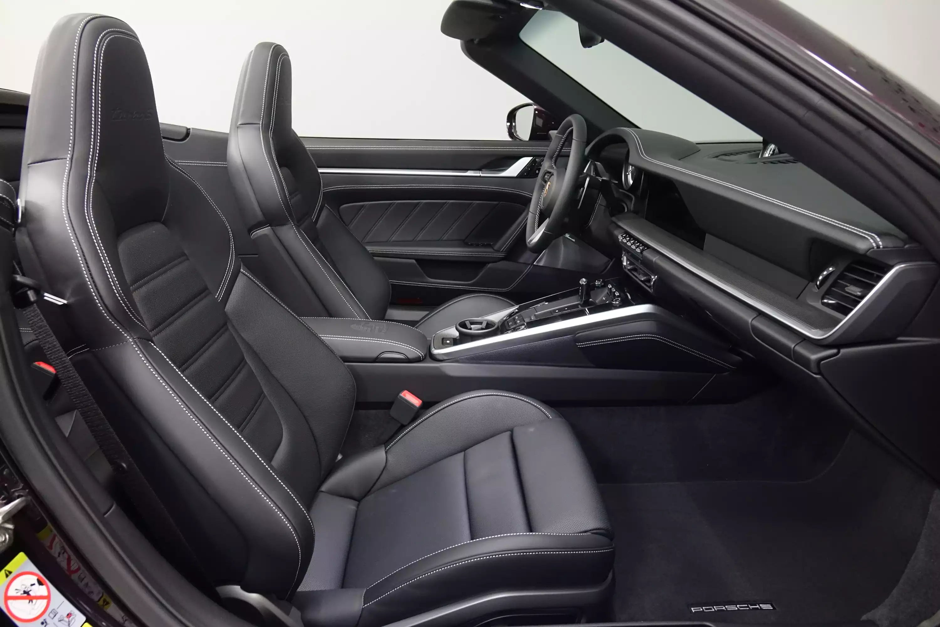 Black leather interior of a Porsche sports car, showing the front bucket seats, steering wheel, center console, and dashboard.