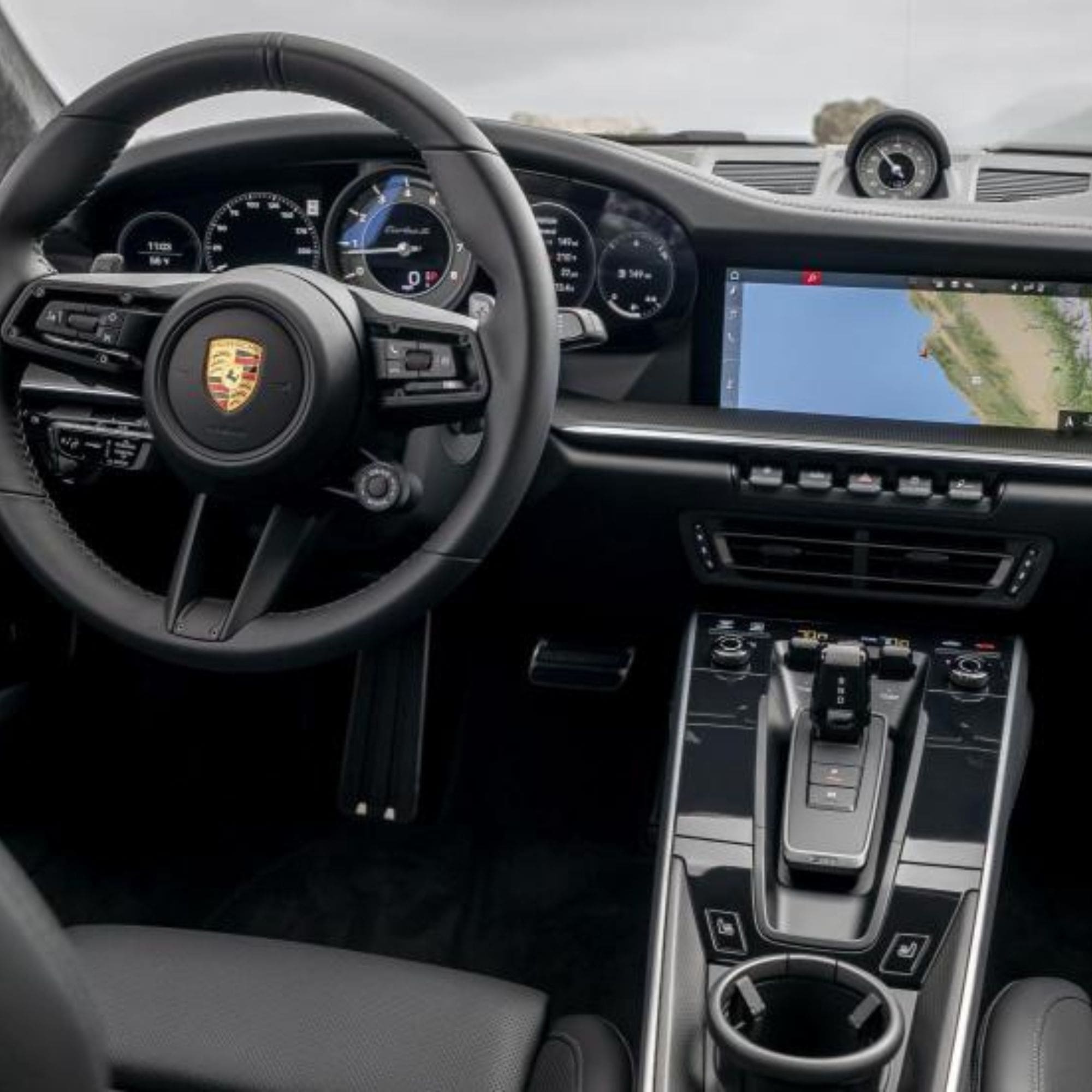 Car interior with steering wheel and dashboard featuring a Porsche logo.