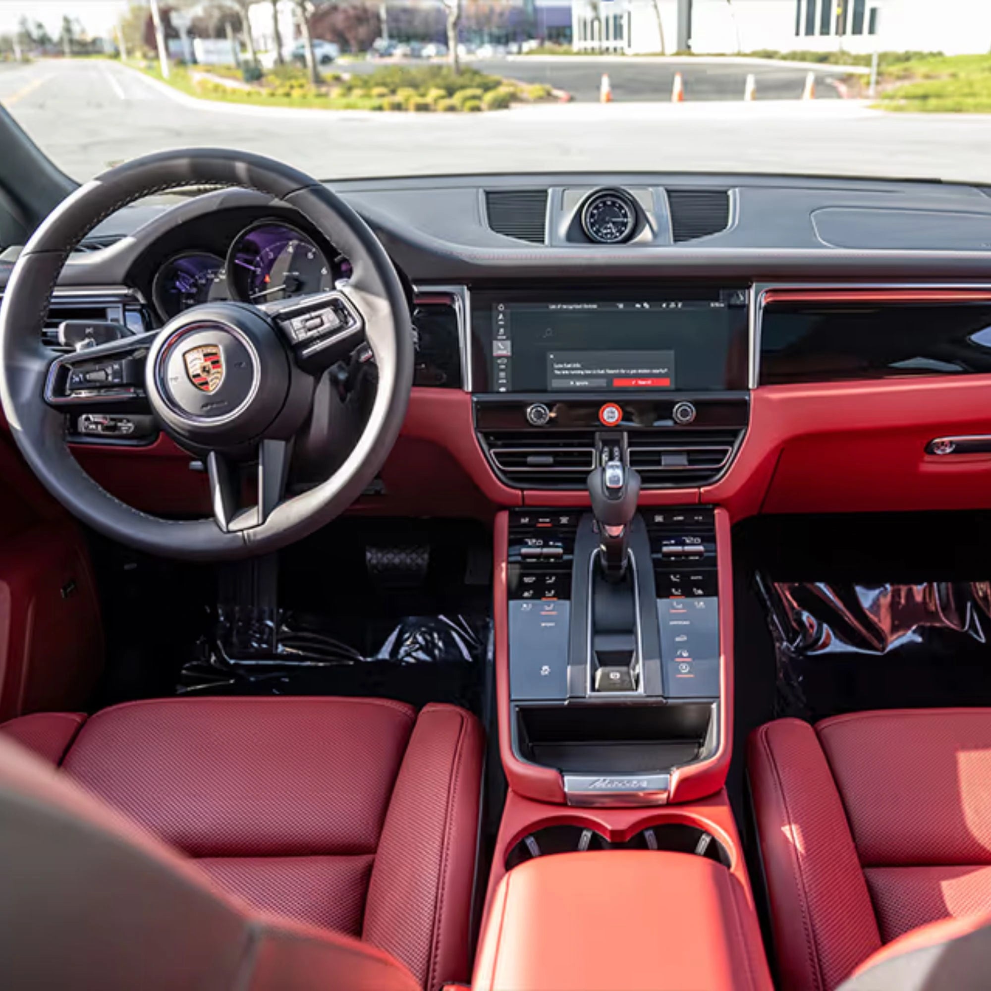 Car interior with red leather seats and a Porsche logo on the steering wheel.