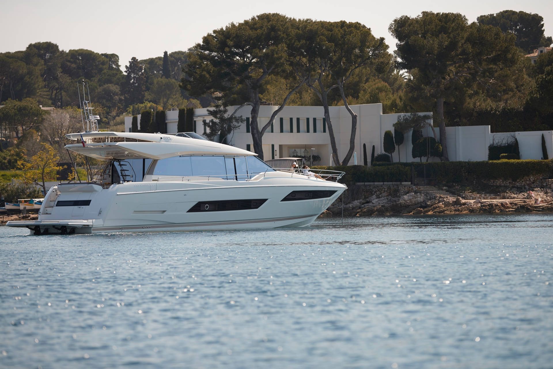 White yacht on water with a building and trees in the background