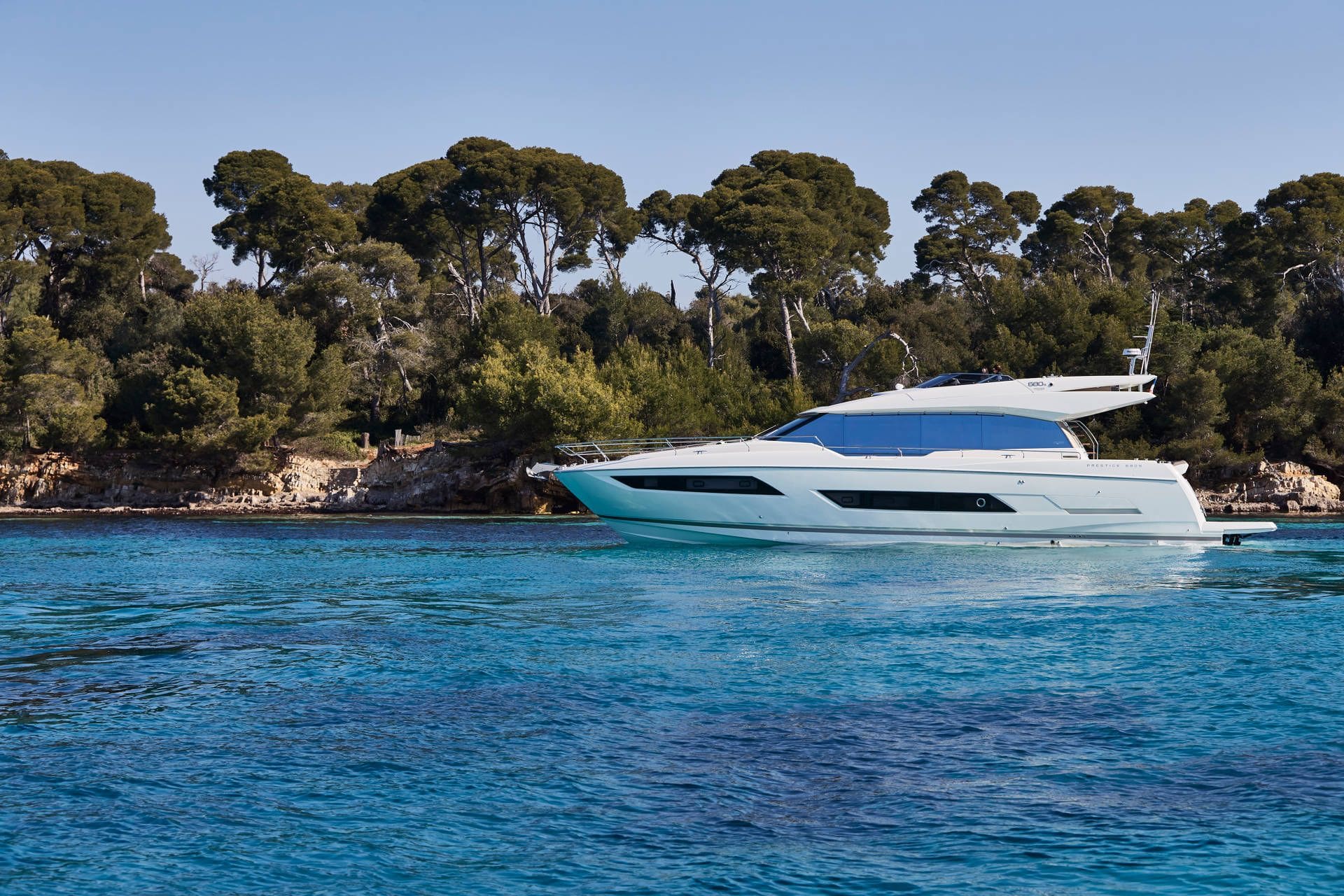 White yacht on a clear blue sea with green trees in the background