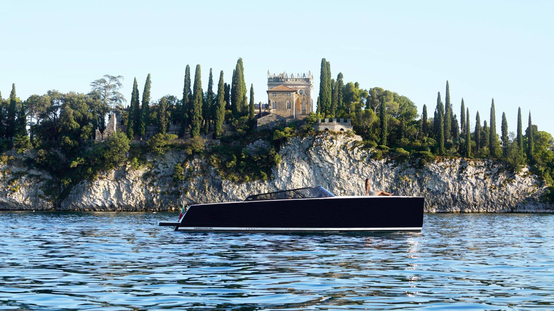 Black boat on water with a scenic background of trees and a castle.