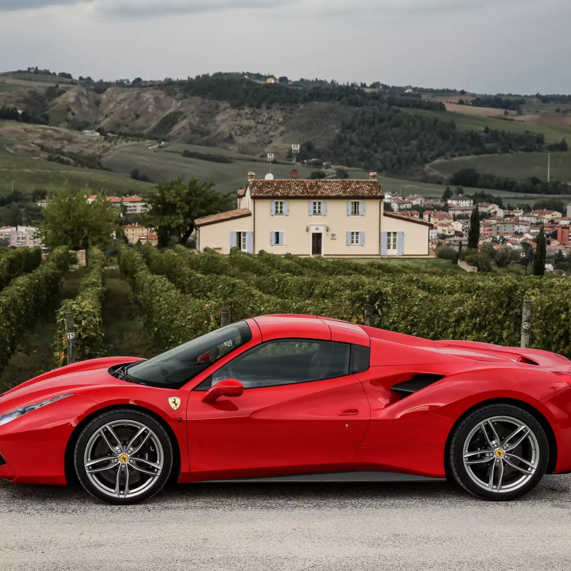 Red sports car parked on a scenic road with a house and landscape in the background