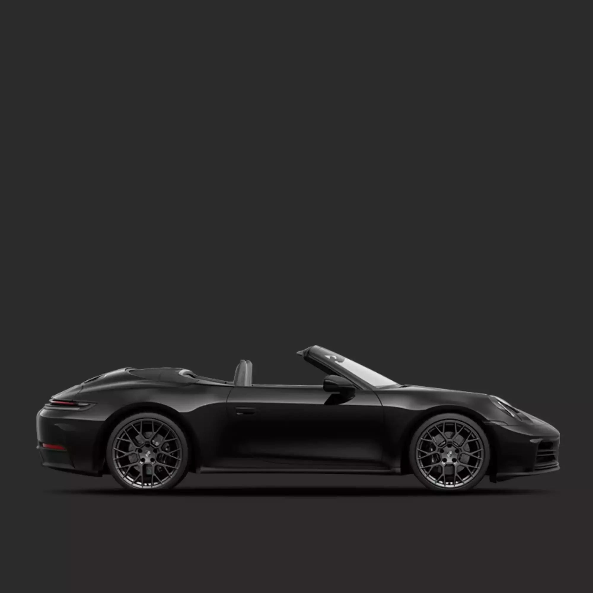 A matte black Porsche 911 Carrera convertible sports car shown in a side profile view against a dark gray studio background.