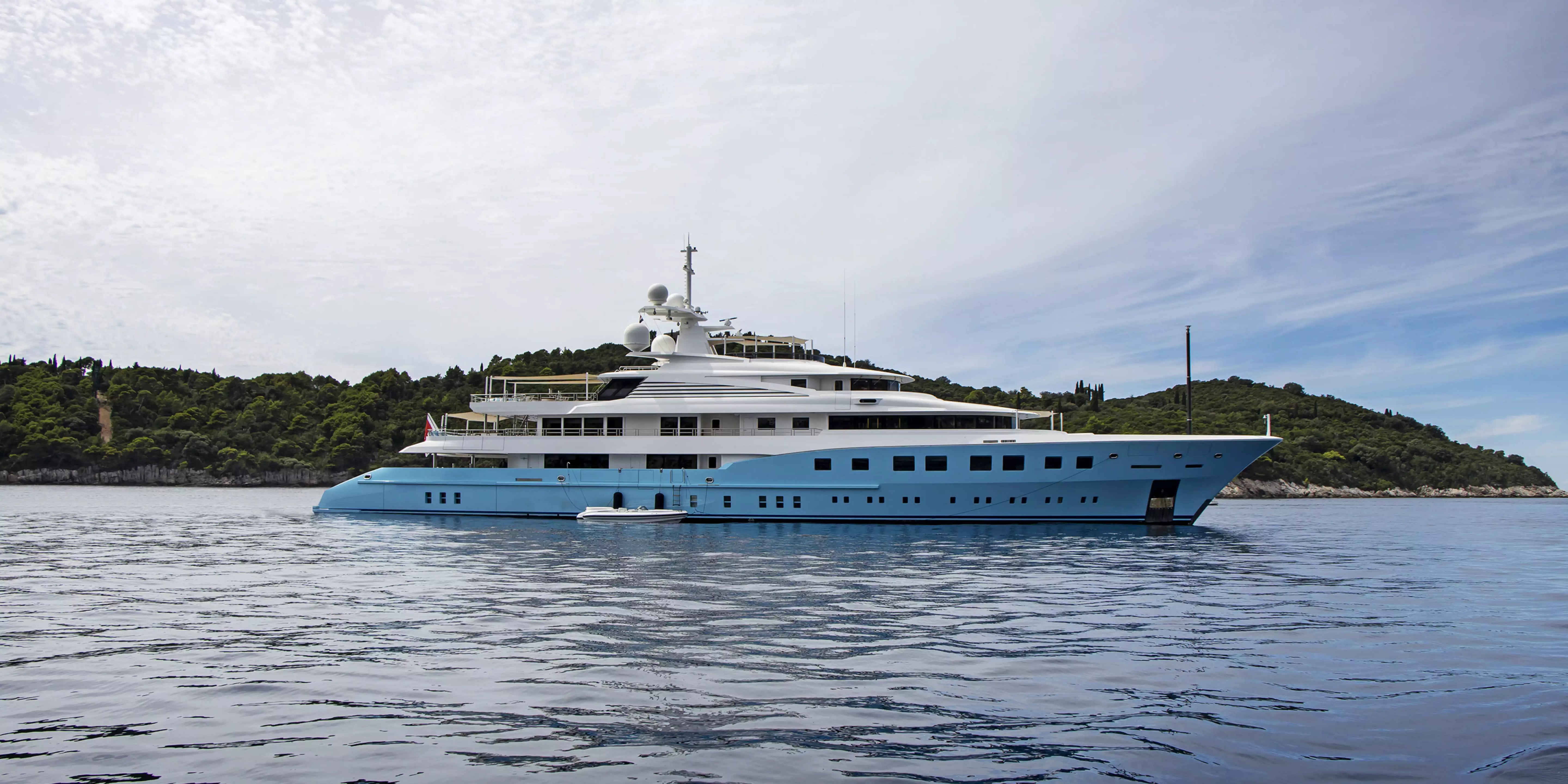 Large blue and white yacht on calm water with a cloudy sky