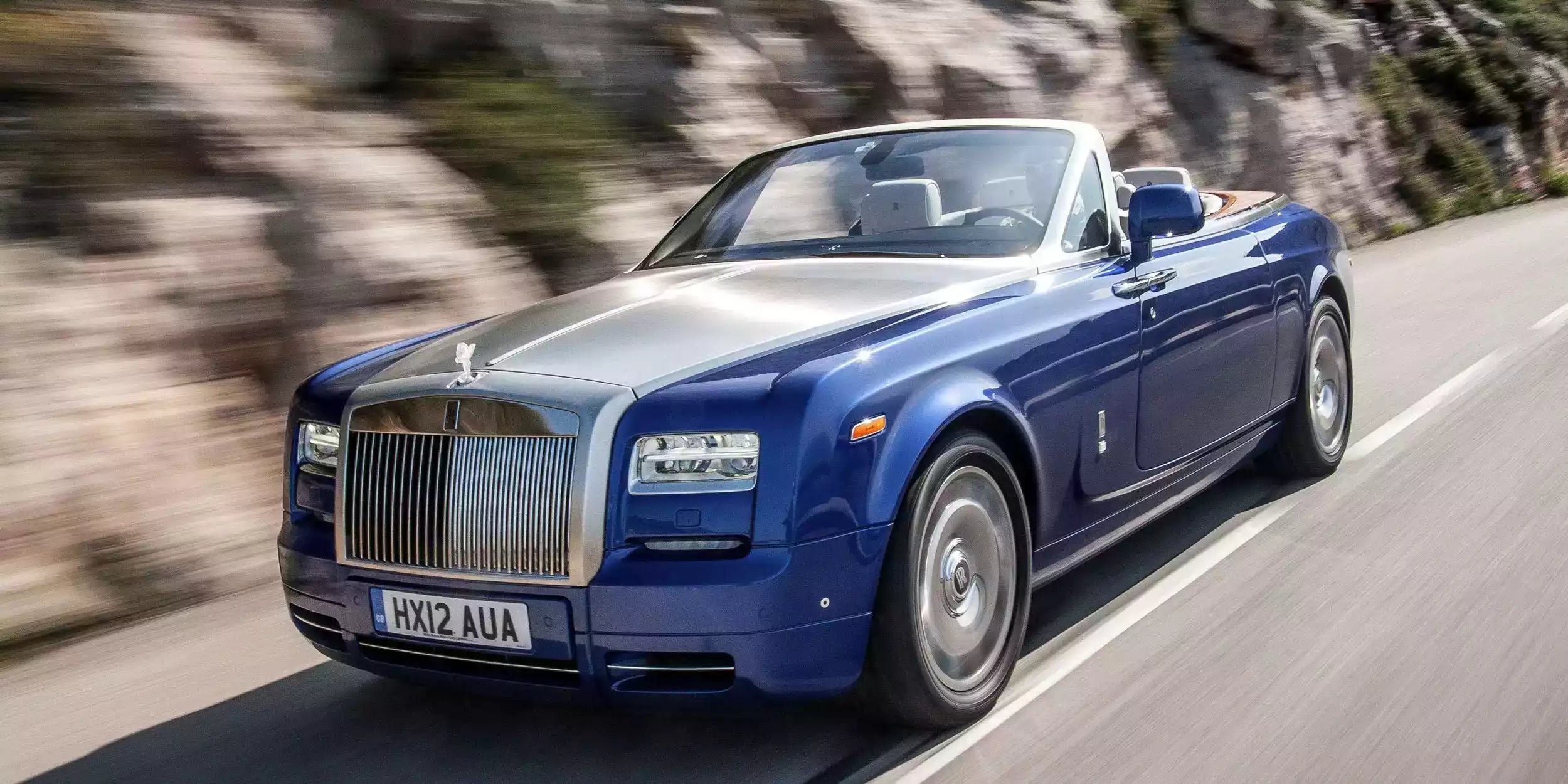 Blue Rolls-Royce convertible driving on a road with blurred background