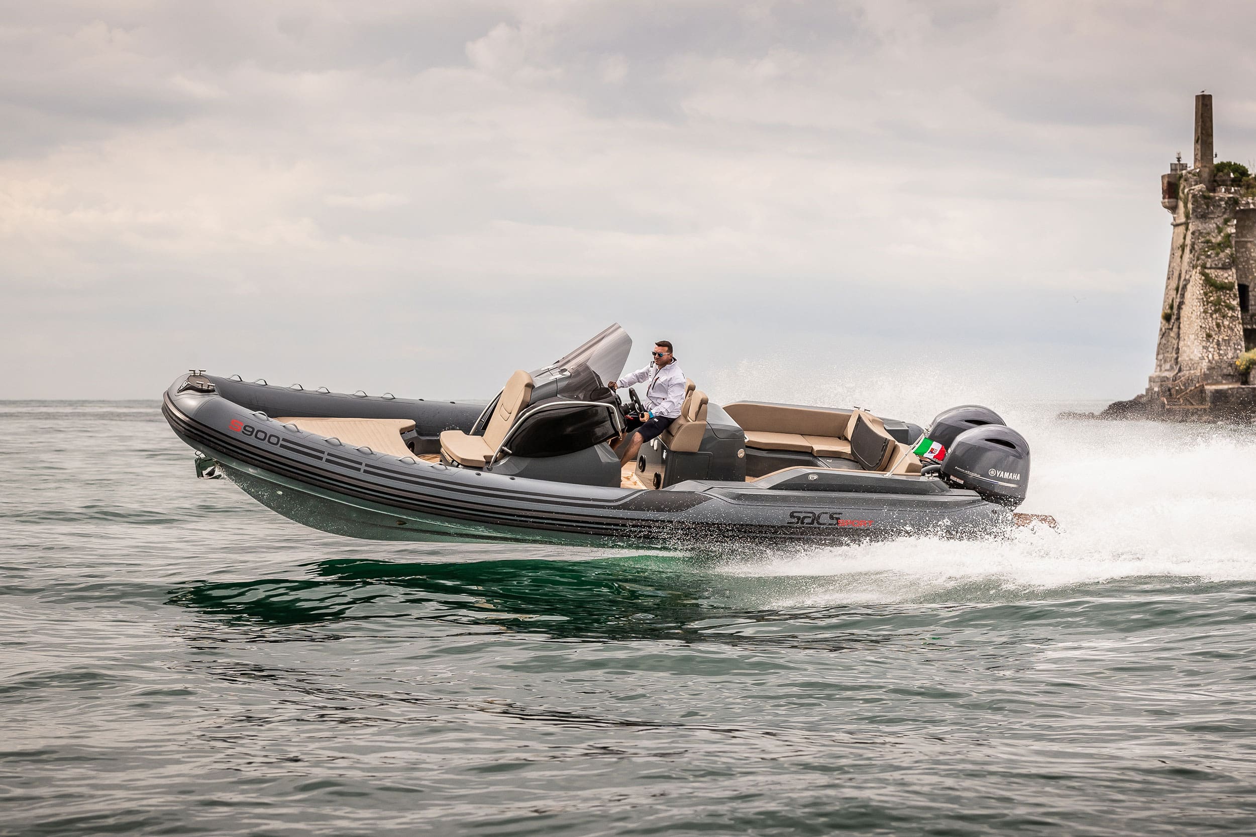 Rigid inflatable boat speeding on water with a person steering, against a backdrop of a castle.