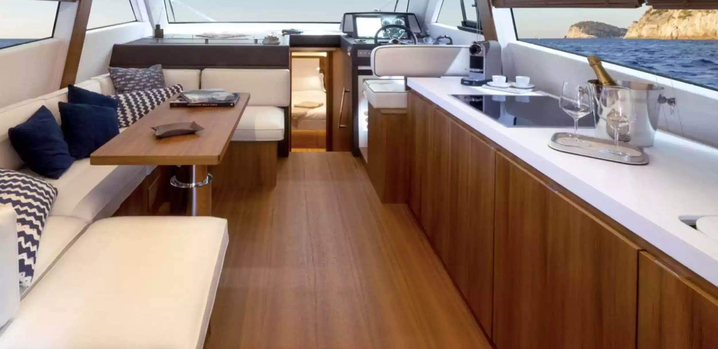 Interior of a boat with wooden floor, white couch, and kitchen area.