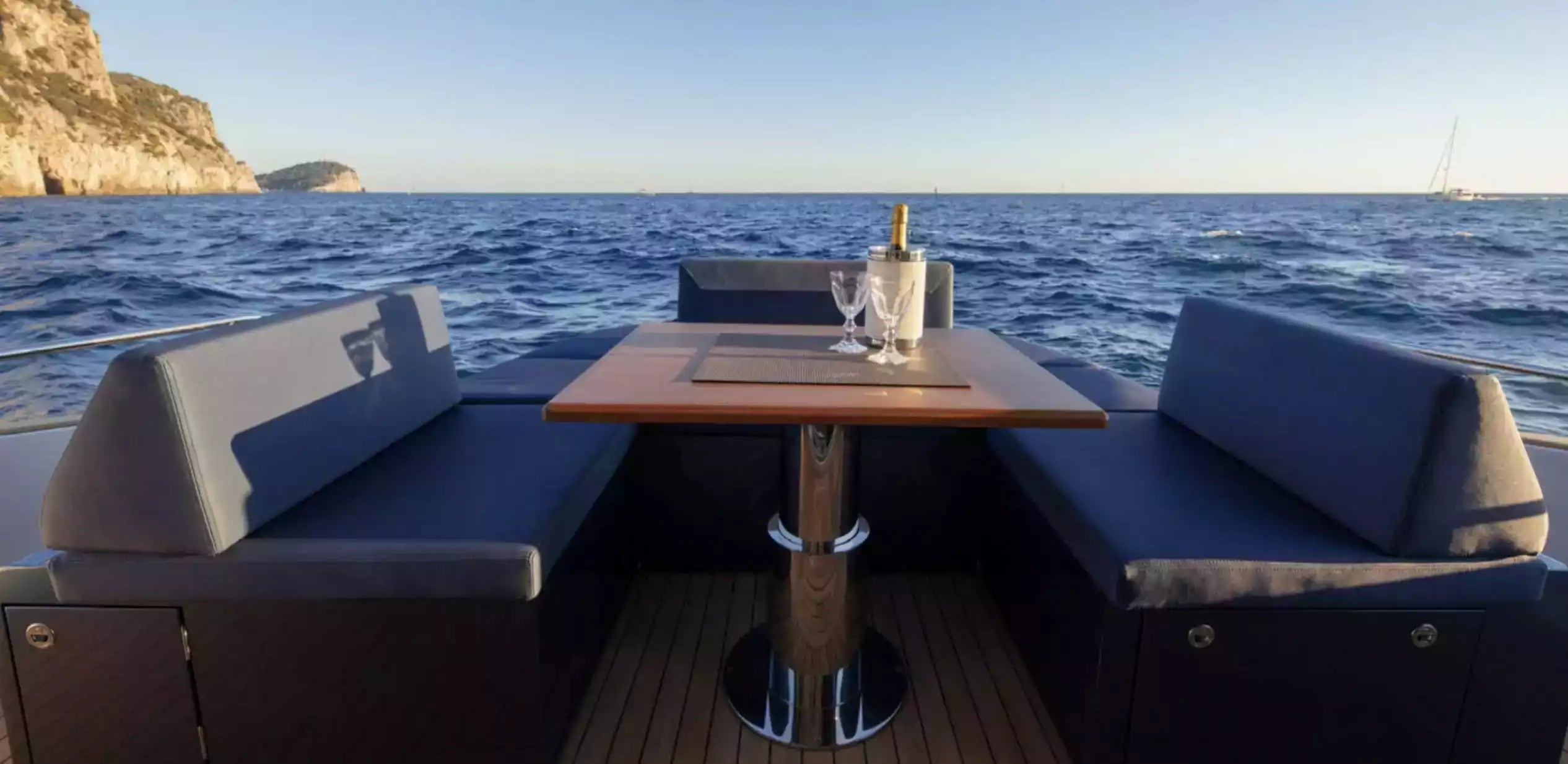Boat interior with table and chairs on a body of water with mountains in the background