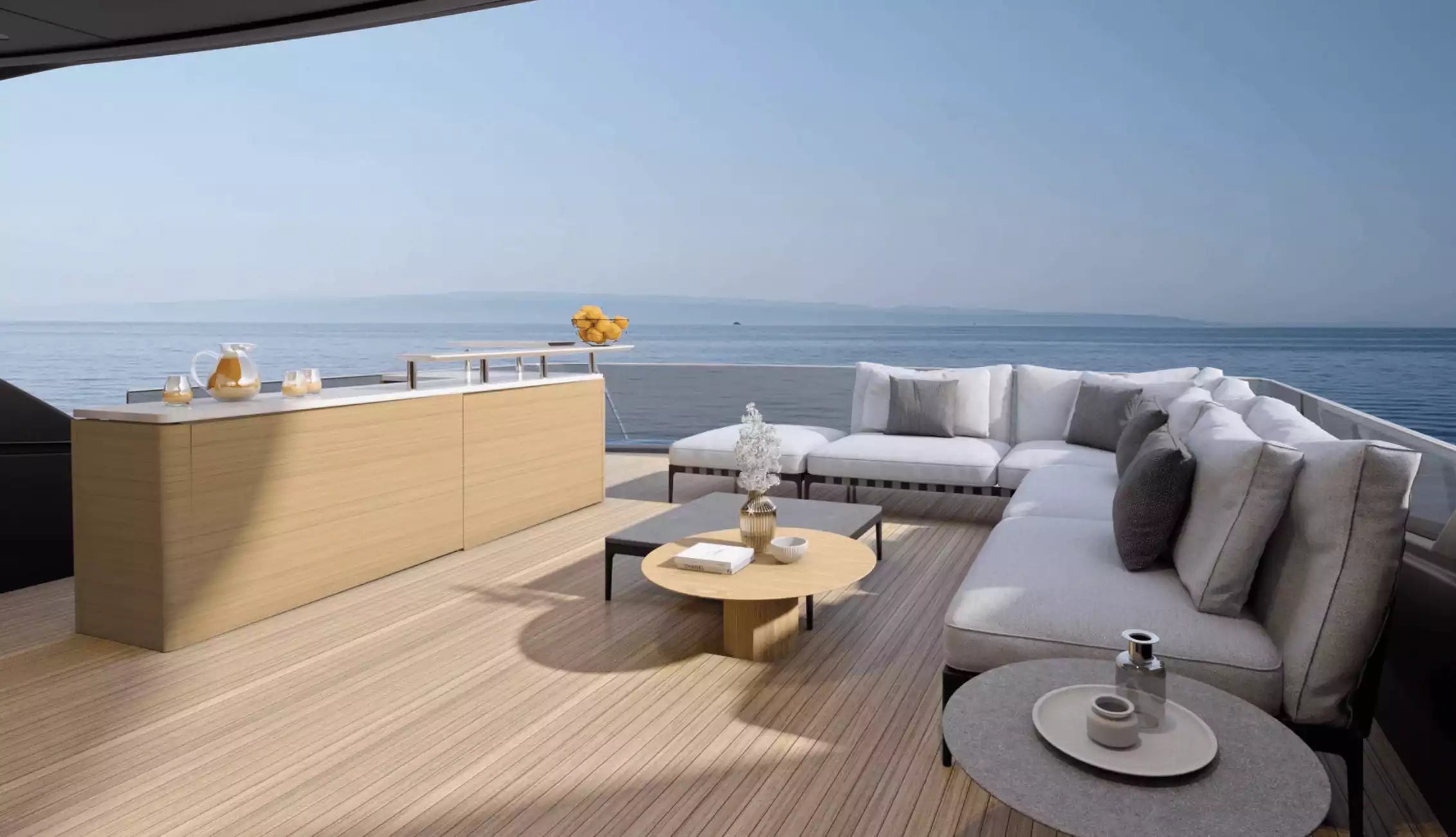 Modern outdoor living space with a sectional sofa, coffee table, and kitchen island overlooking the ocean.