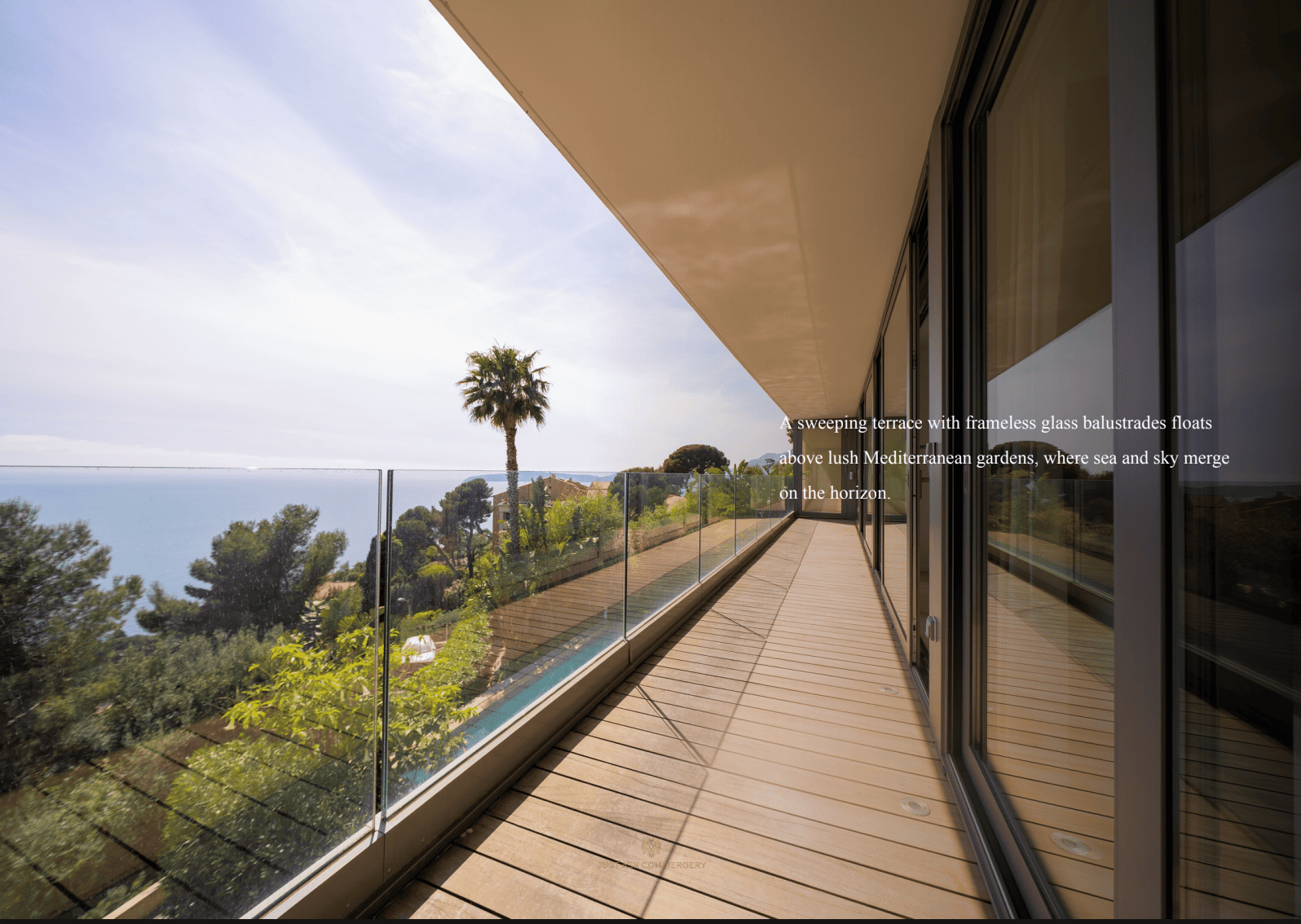 Modern balcony with glass railings overlooking a scenic view of trees and sea.
