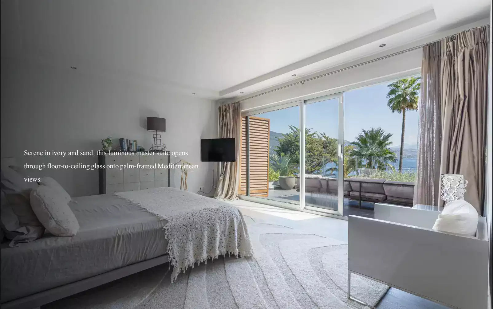 Modern bedroom with a large window view of palm trees and ocean.
