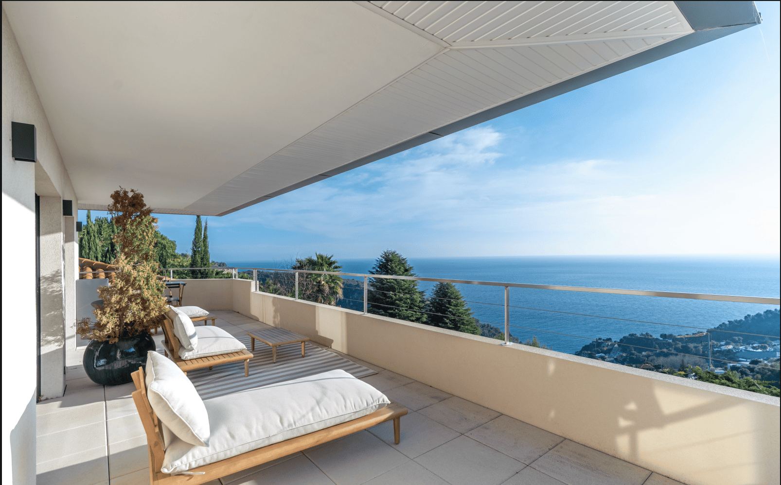 Modern balcony with ocean view, featuring a wooden bench and white cushions.