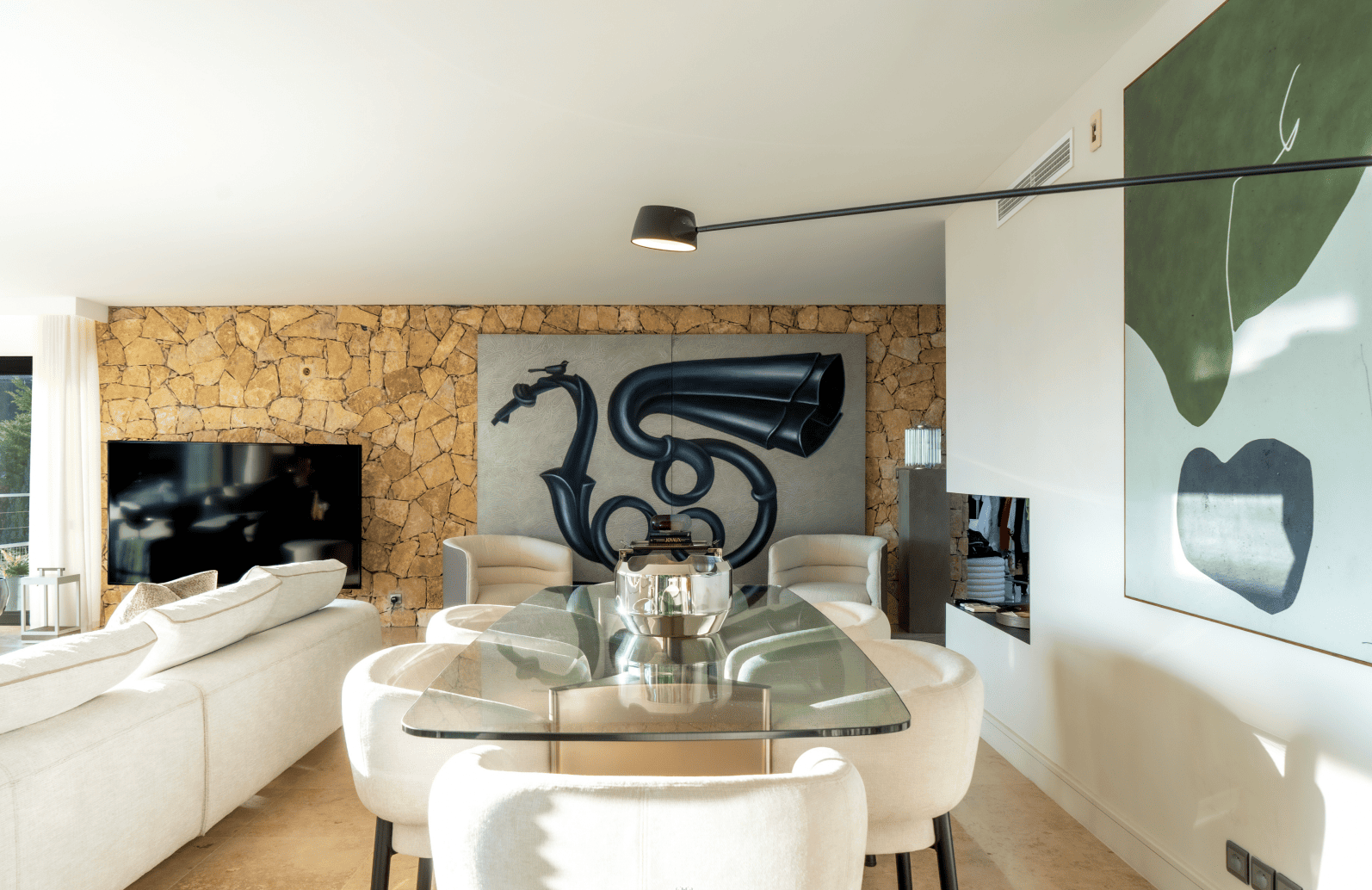 Modern living room with a glass dining table and white chairs, featuring a decorative wall piece.