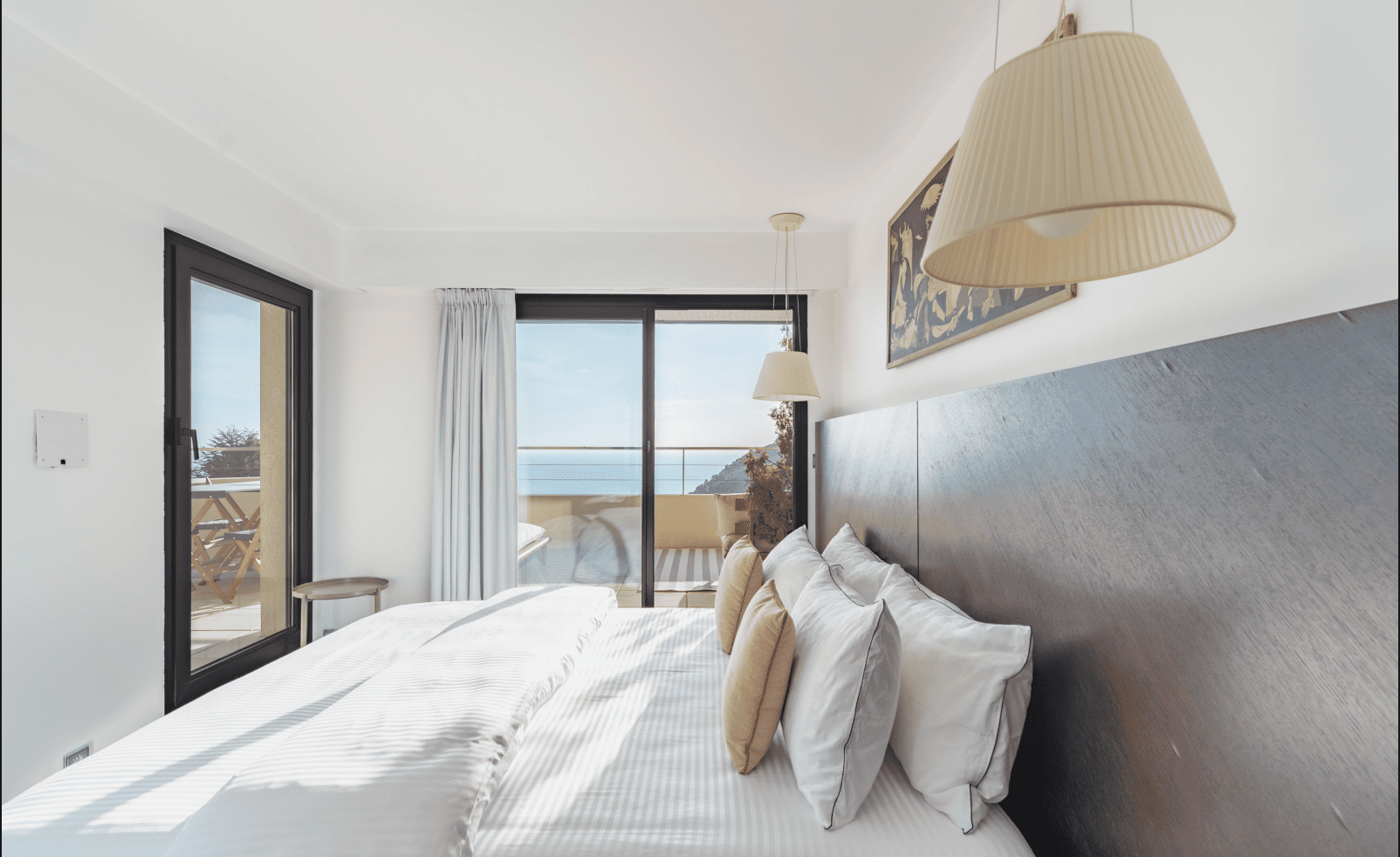 Modern bedroom with a large bed, pillows, and a view of the ocean through a window.