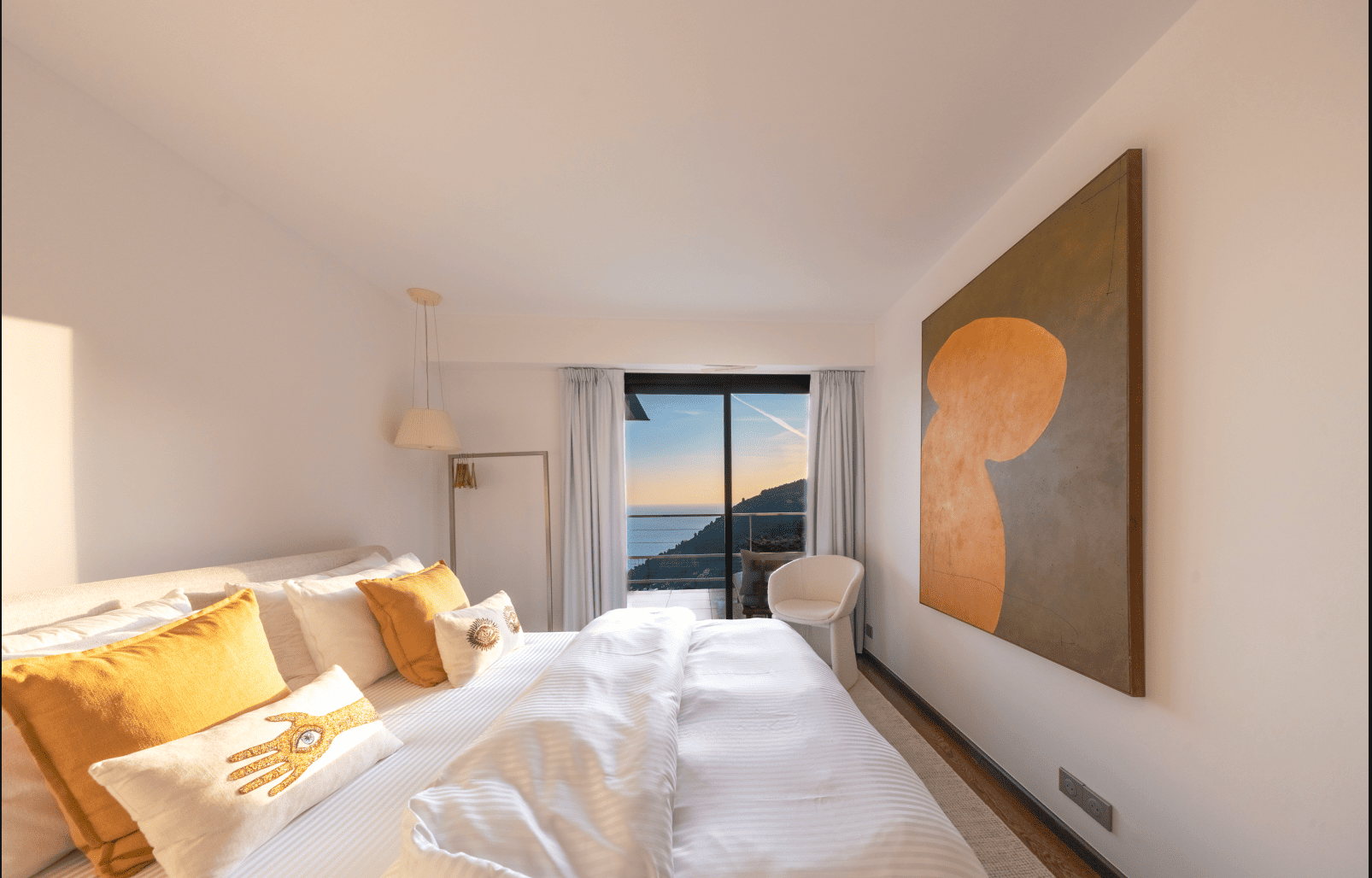 Modern bedroom with a bed, abstract art, and a view of the ocean.