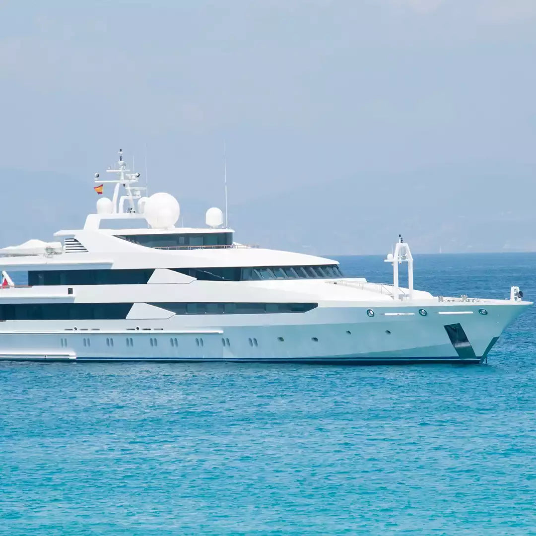 A large white luxury yacht floating on bright turquoise blue water under a pale sky.