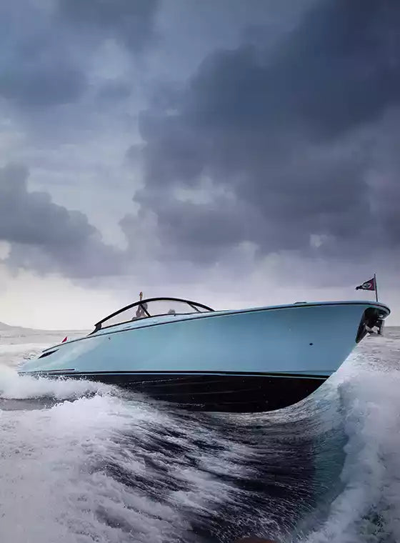 Blue speedboat cutting through water with a stormy sky in the background