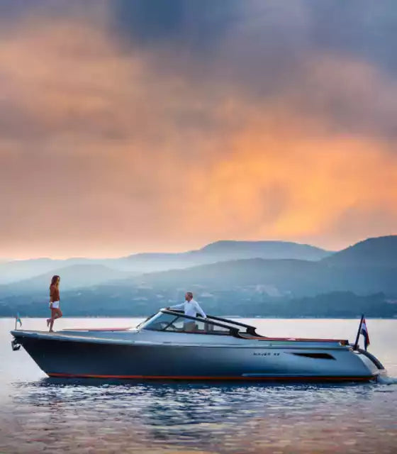 Two people on a boat with a scenic background of mountains and sunset.
