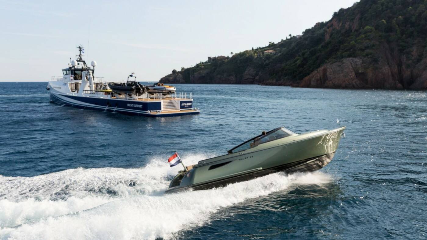 Speedboat cutting through water with a ferry in the background on a coastal landscape.