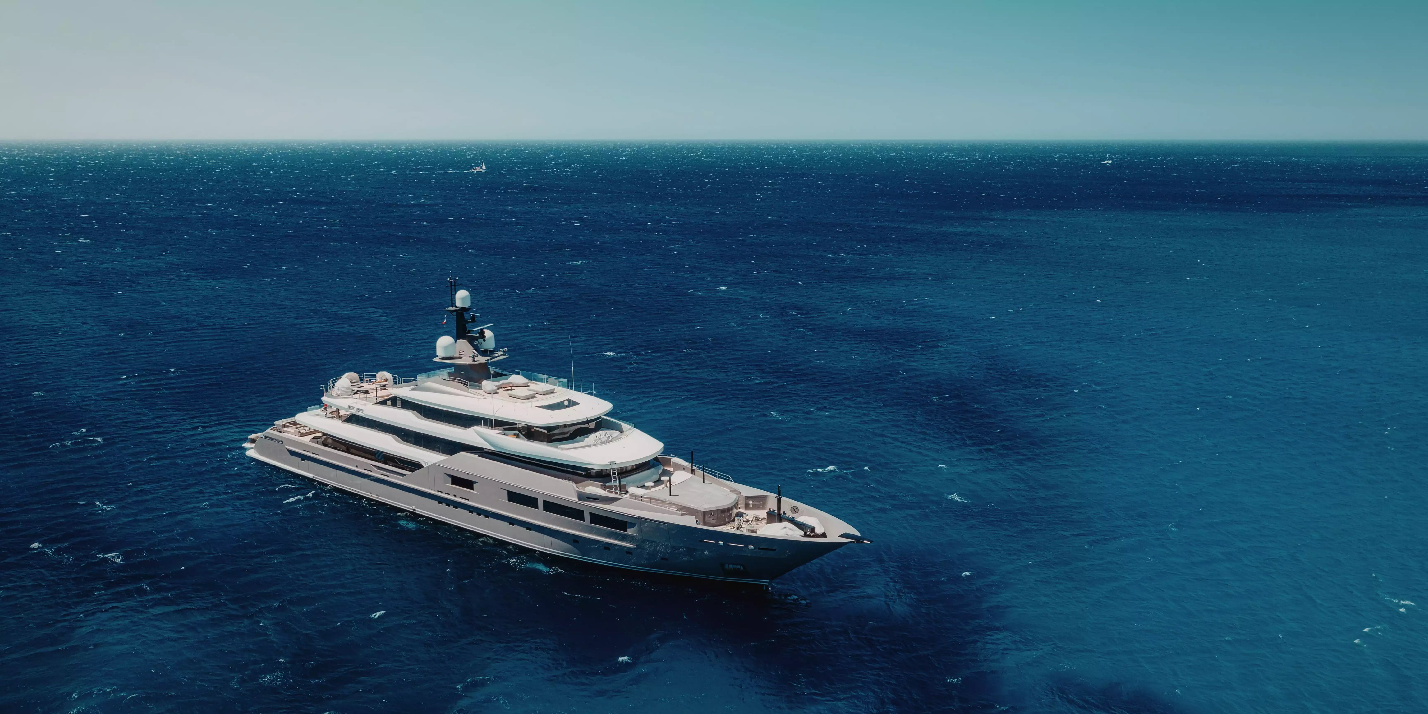 Luxury yacht sailing on a calm blue ocean with clear skies.