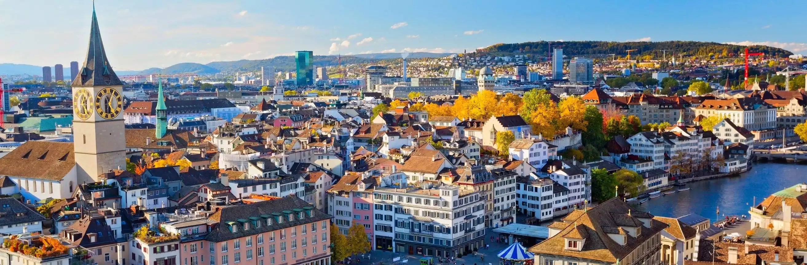 Cityscape with historic buildings and a clock tower, featuring a mountain in the background.